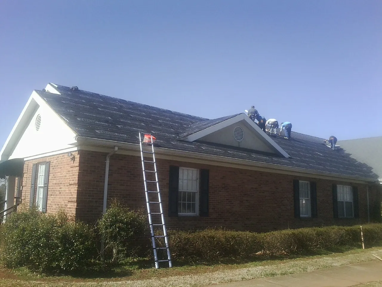 Crew tearing shingles off a brick ranch roof with a ladder set — Metal Roof Repair work by our crew in Thornville