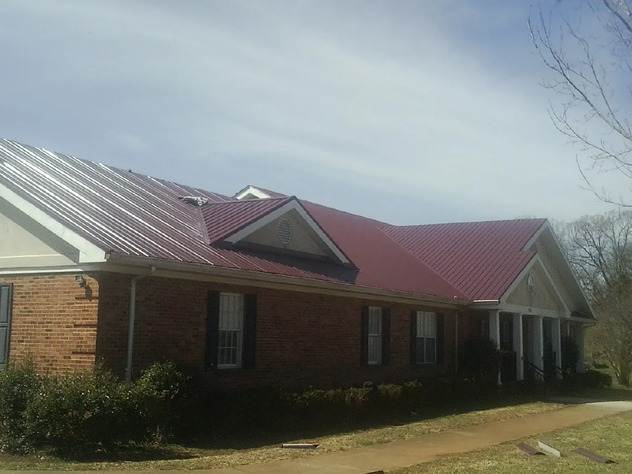 Red metal roof with gabled entries on a long brick building, from a Hail Damage Roof Repair job in Thornville
