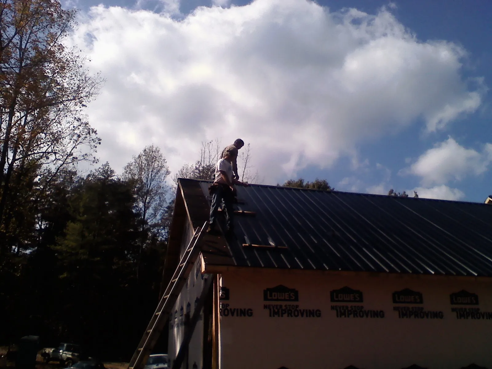 Roofer fastening dark metal panels high against a cloudy sky, from a Roof Inspection job in Thornville