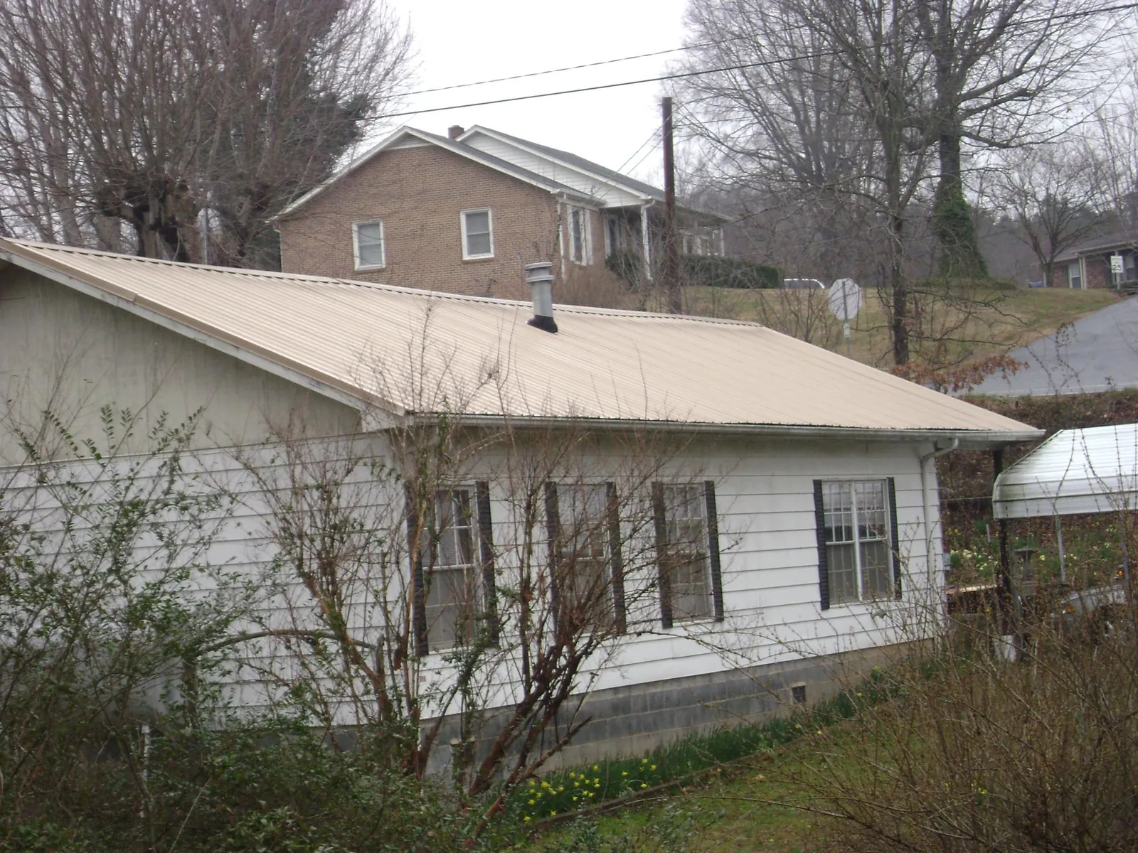 Tan metal roof on a white sided house set into a hillside — Commercial Roofing by Roofing Brothers in Thornville